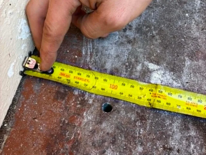 Measuring a slab edge with a tape measure during a termite risk check on a Perth home
