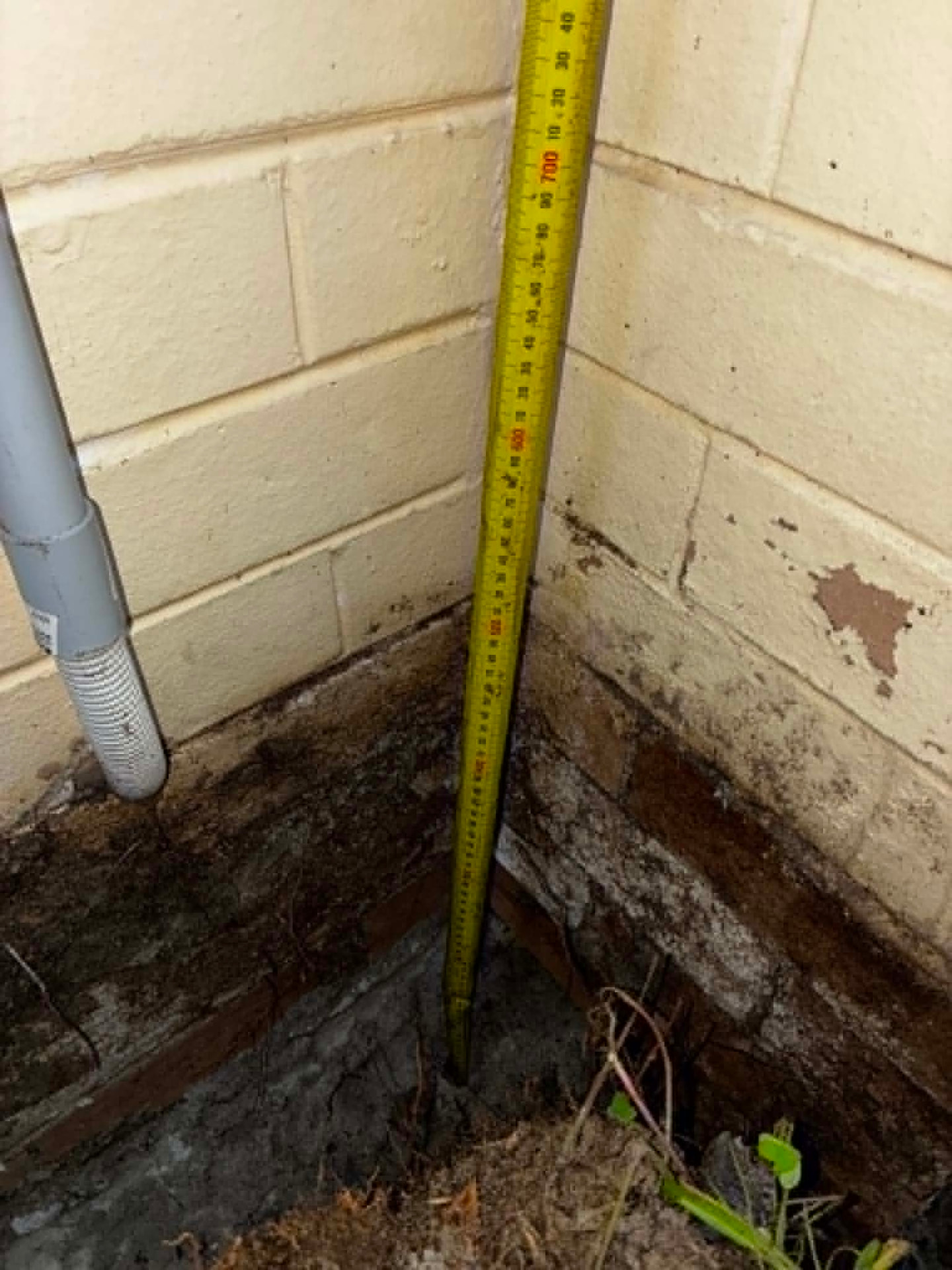 Excavated corner showing a concealed slab edge previously covered by soil against a brick wall